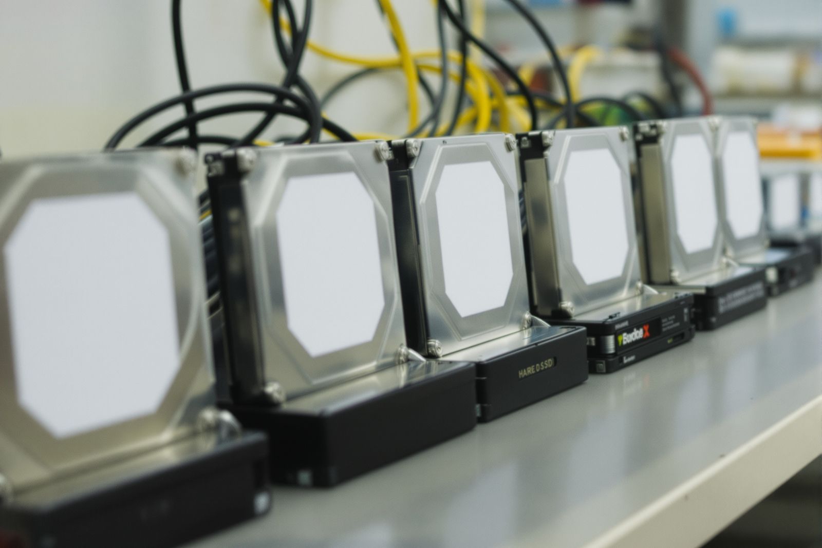 PLACEHOLDER — shot list for the real photographer: a row of bare hard drives and SSDs standing on a workbench, cables coiled behind, blank unlabelled tops
